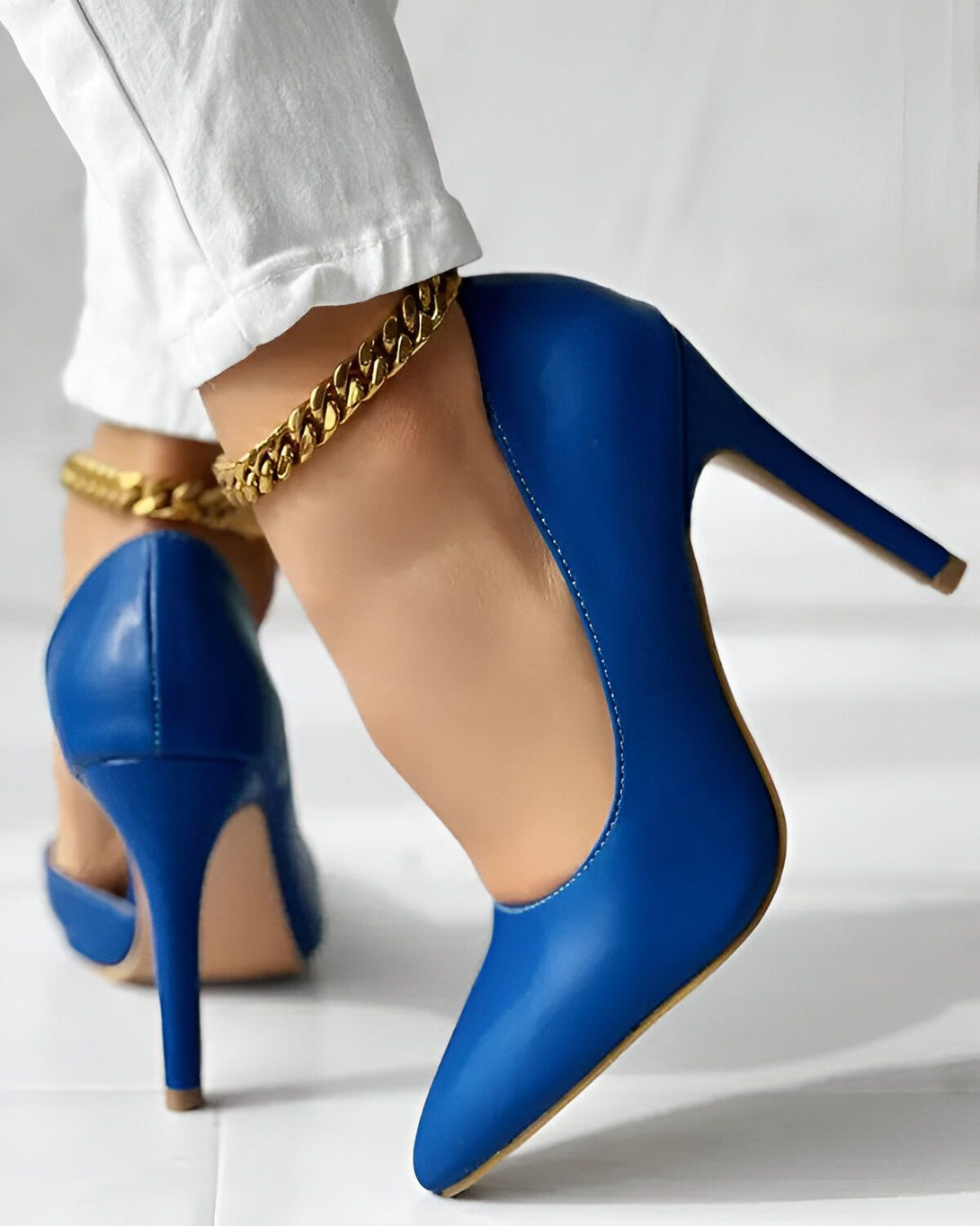 Une femme porte des escarpins bleus à talons hauts. Elle porte également une chaîne dorée autour de la cheville.
