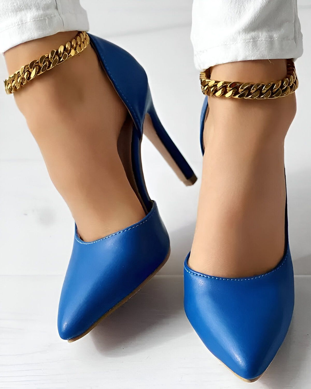 Une femme porte des escarpins bleus à talons hauts et des chaînes dorées aux chevilles.