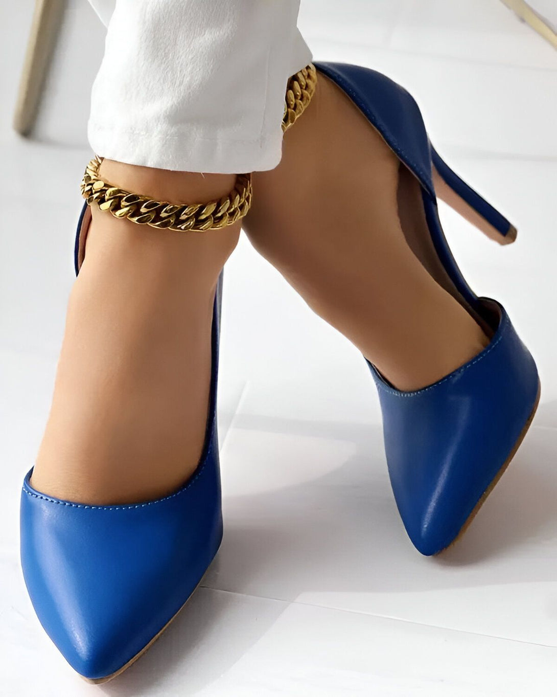 Une femme porte des escarpins bleus à talons hauts et un bracelet de cheville en or.