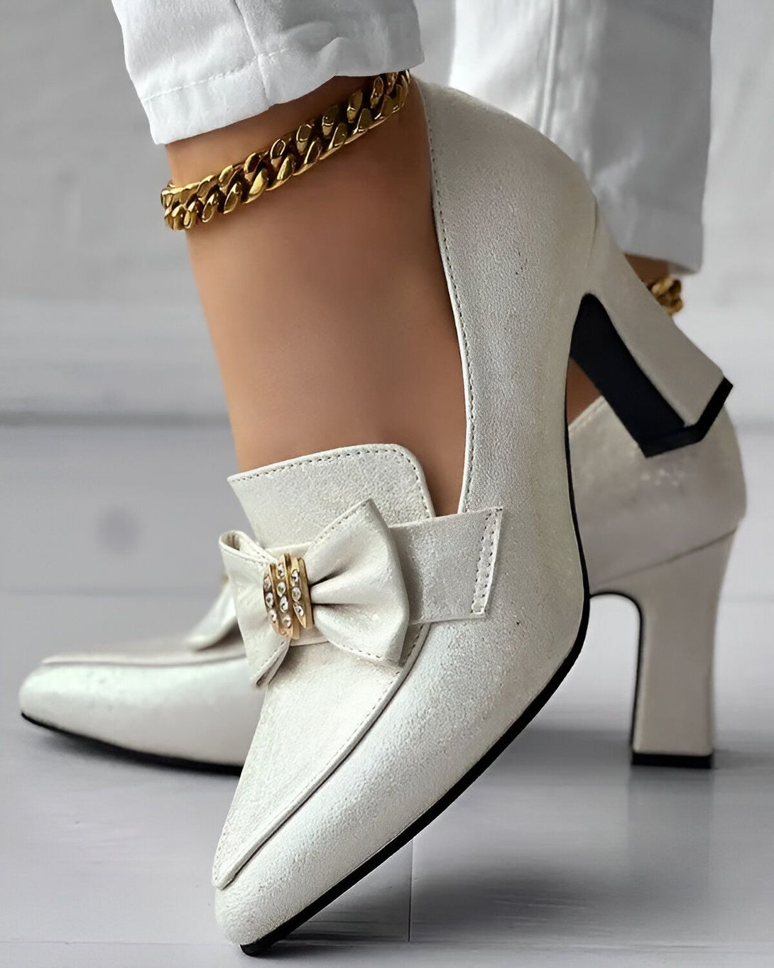 Une image d'une paire d'escarpins blancs à talons hauts avec un nœud sur le devant. Les chaussures sont portées par une femme qui porte un pantalon blanc et une cheville dorée.