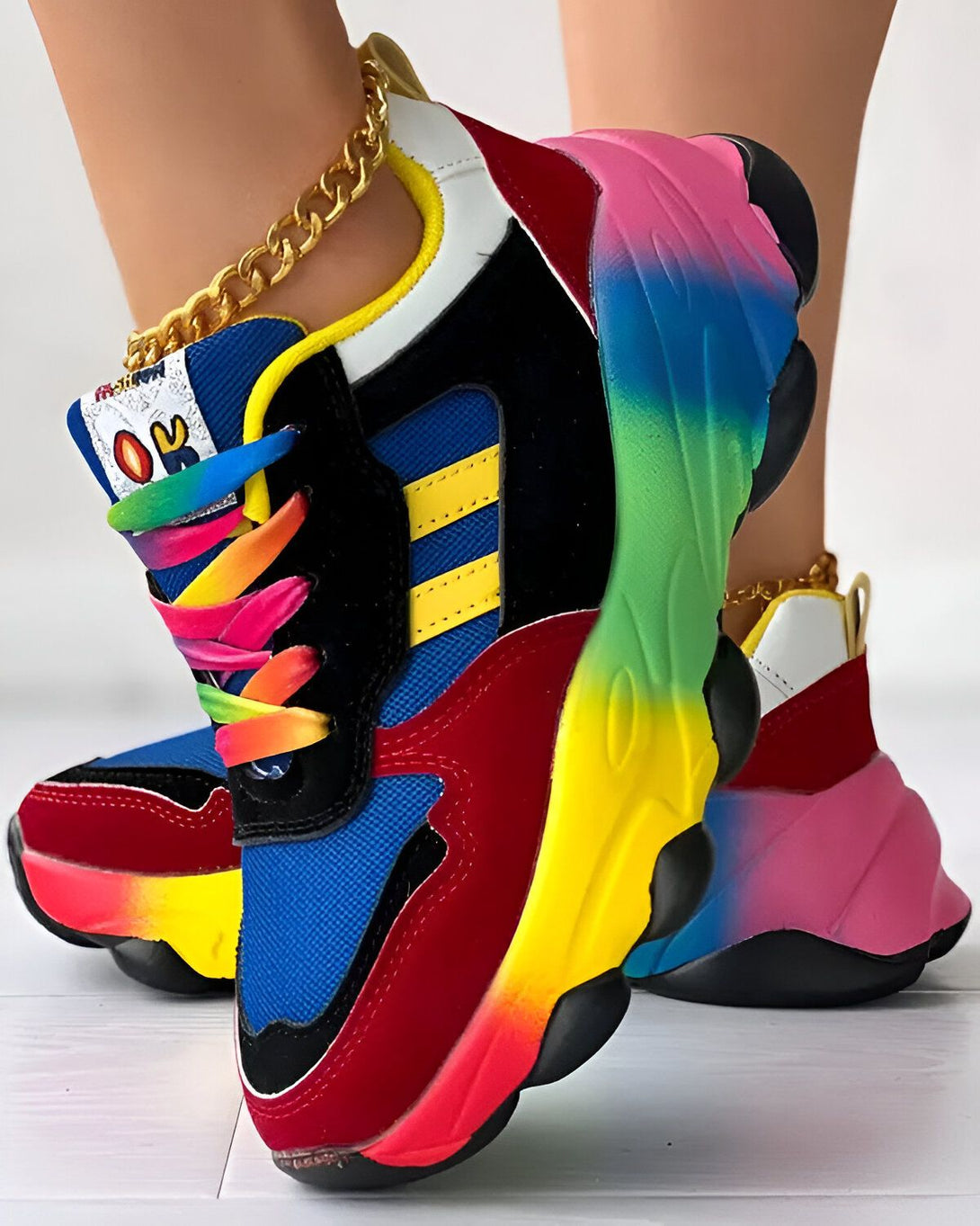 Une paire de baskets multicolores avec des lacets arc-en-ciel et une chaîne dorée sur la cheville.