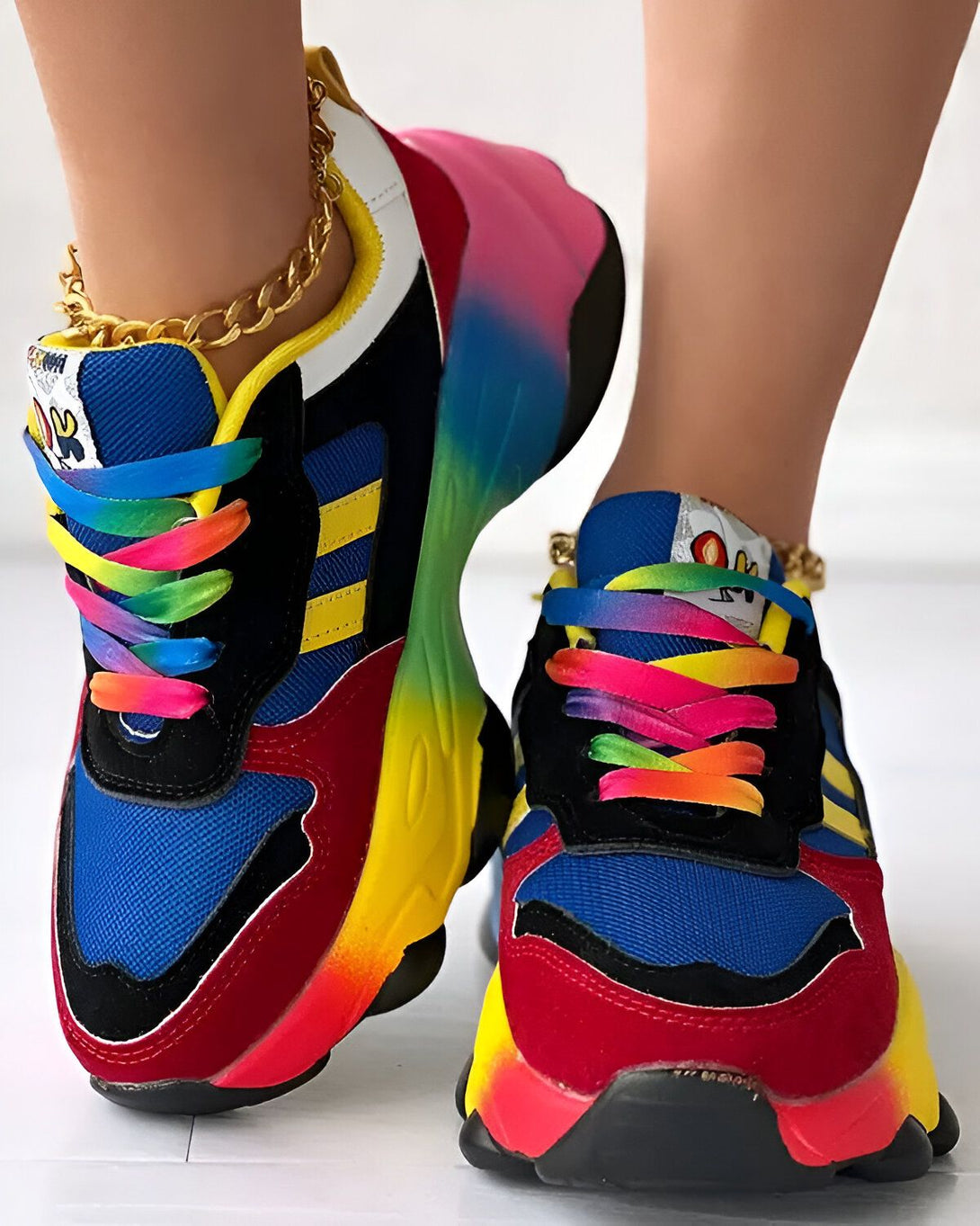Une femme porte des baskets multicolores avec des lacets arc-en-ciel. Les baskets sont bleues, jaunes, rouges et noires. La semelle est blanche.