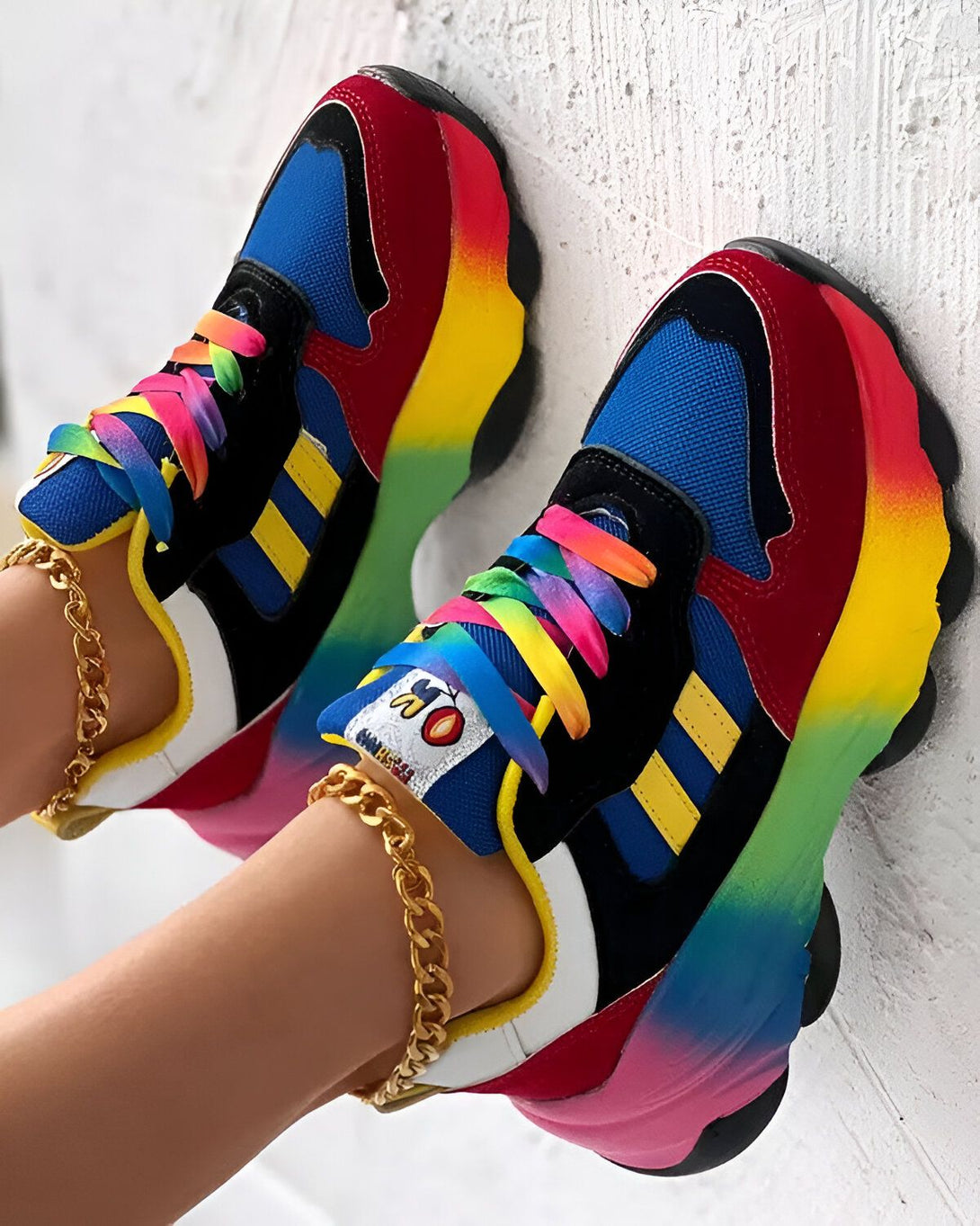 Une paire de baskets multicolores avec des lacets arc-en-ciel sur un fond blanc.