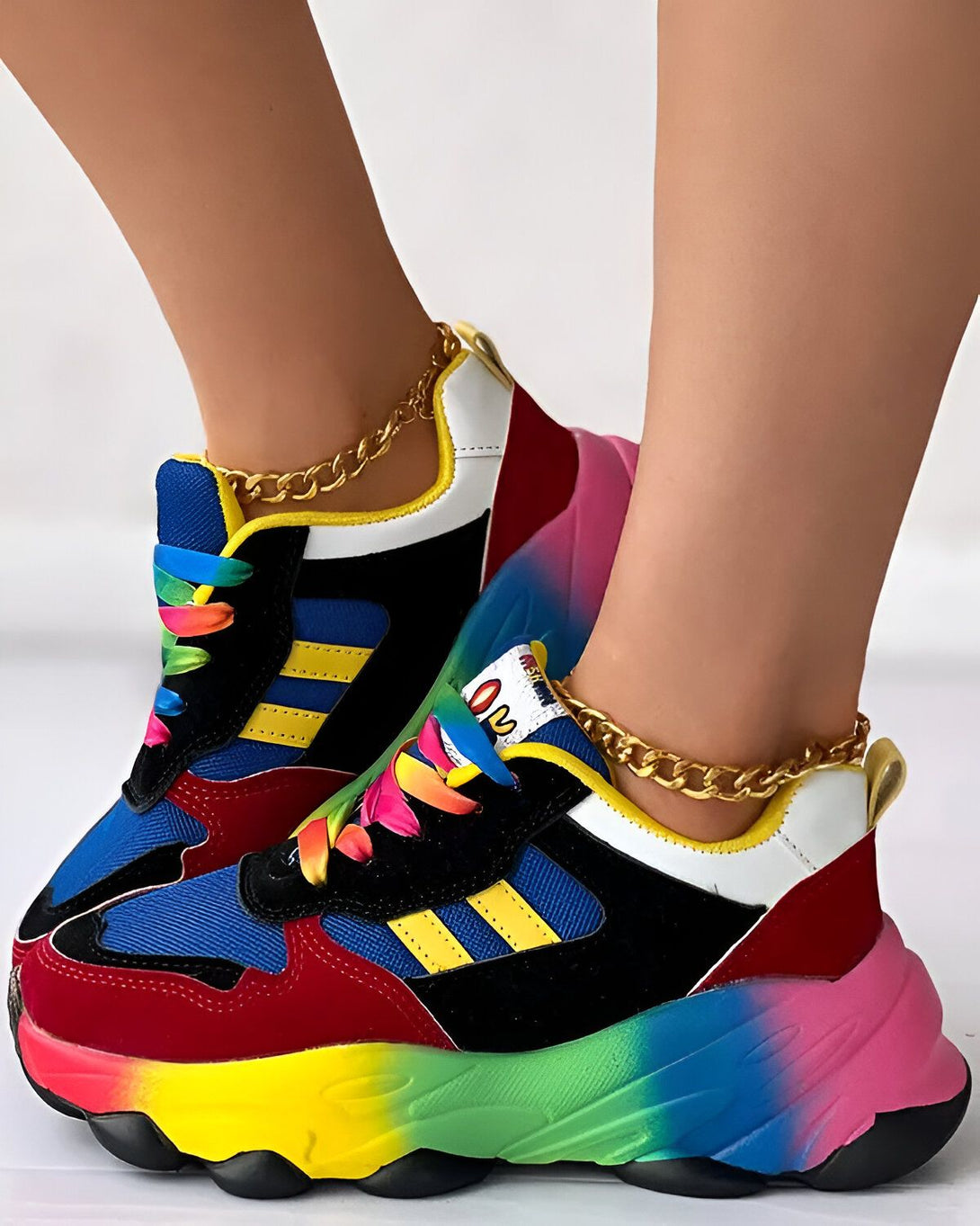 Une paire de baskets multicolores avec des lacets arc-en-ciel et une chaîne dorée autour de la cheville.
