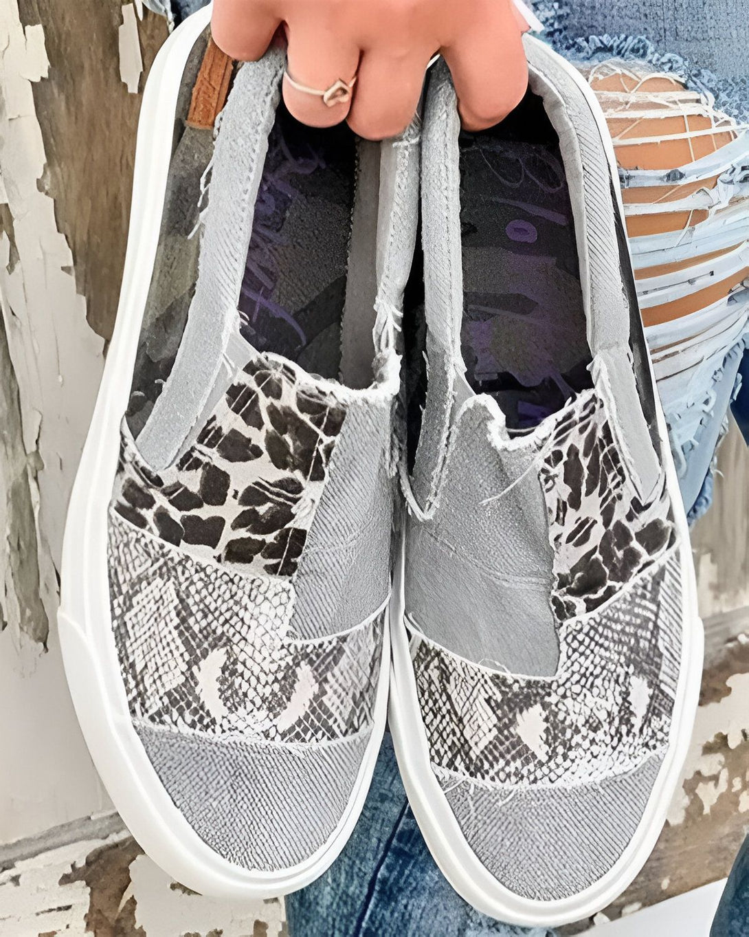 Une image de chaussures slip-on grises et noires avec un motif léopard et serpent. Les chaussures sont portées par une femme qui porte des jeans troués.