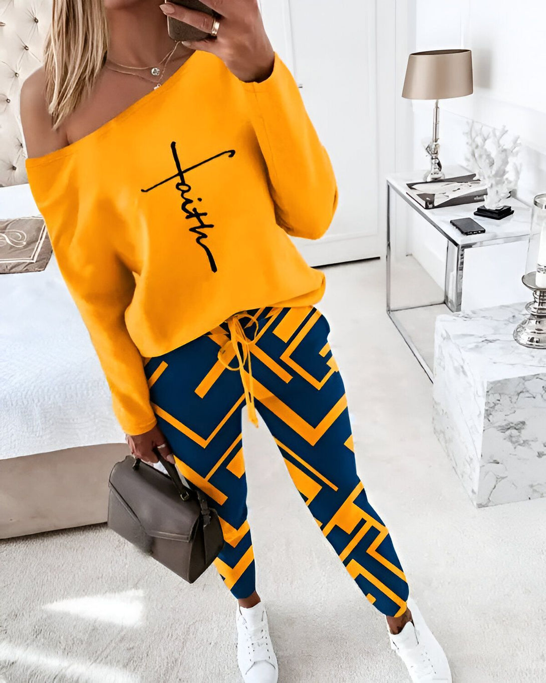 Une femme porte un ensemble de jogging jaune et bleu. Le haut est jaune avec un motif de croix noire sur l'épaule. Le pantalon est bleu avec un motif de losanges jaunes.