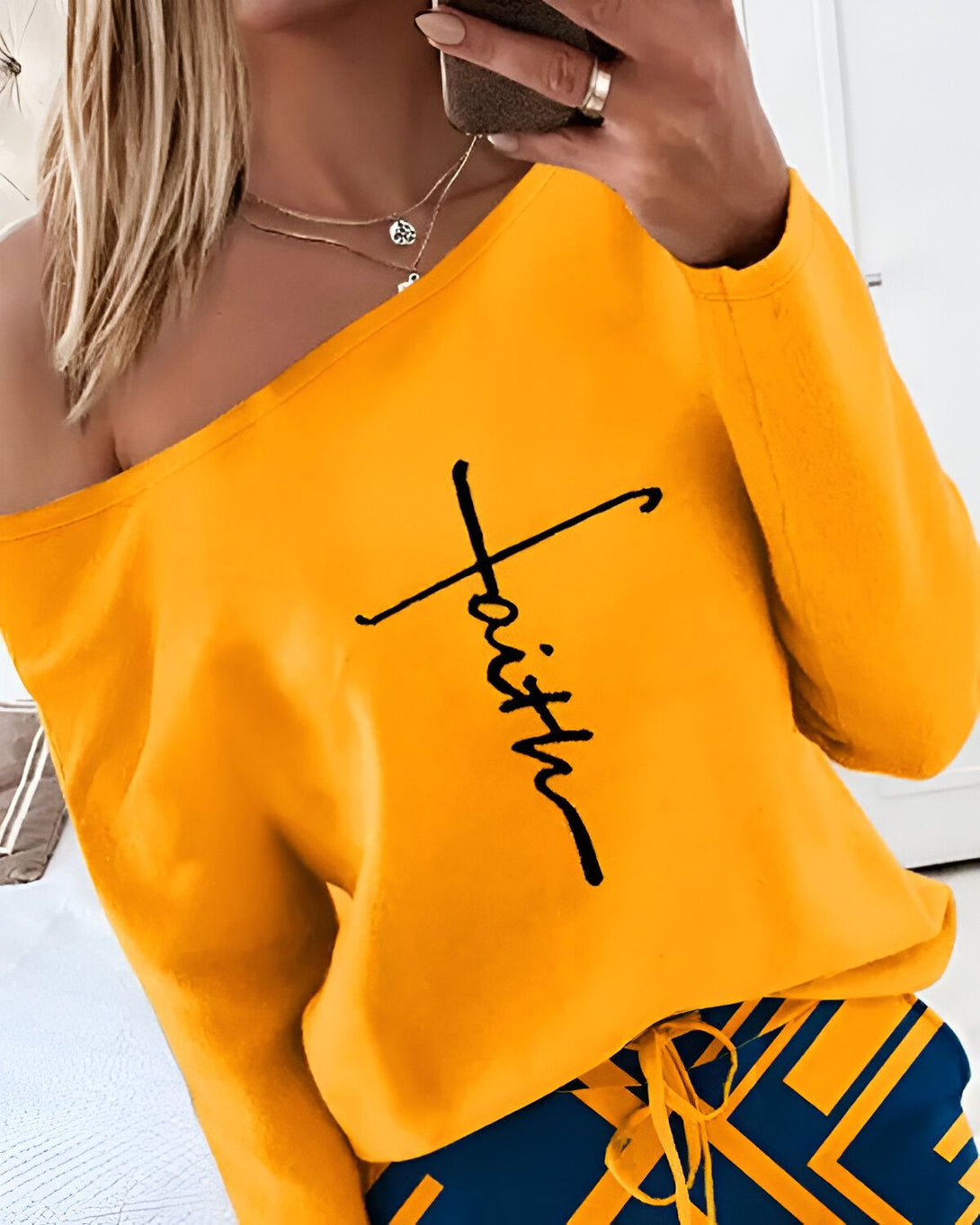 Une femme porte un haut jaune à épaules dénudées avec le mot "faith" écrit en noir sur le devant. Elle porte également un pantalon de jogging bleu et jaune.