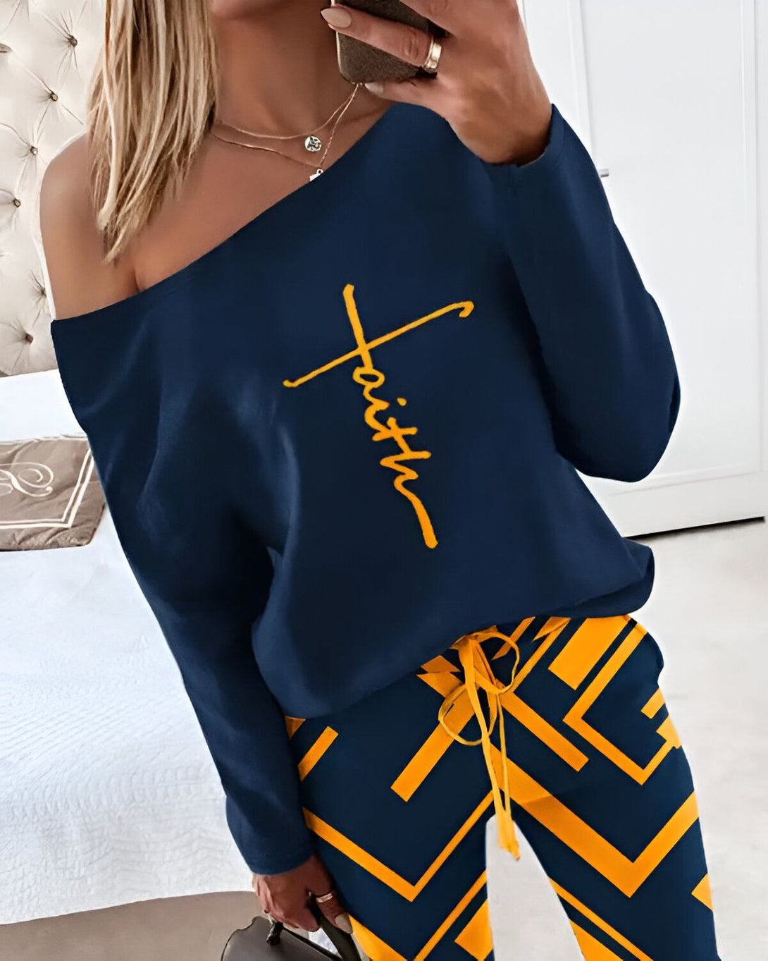 Une femme porte un haut bleu marine à épaules dénudées avec le mot "foi" écrit en jaune. Elle porte également un pantalon jaune et bleu marine à motifs géométriques.