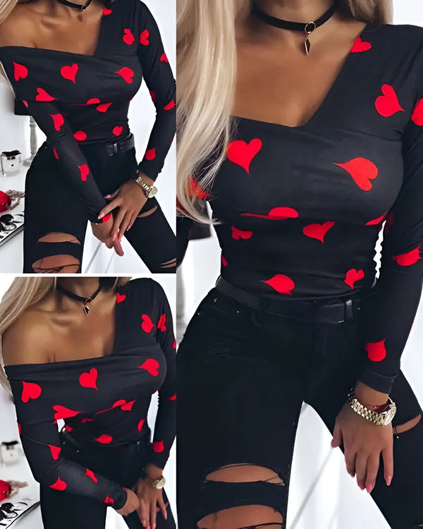 Une femme porte un haut noir à manches longues avec des coeurs rouges. Le haut est décolleté en V et les manches sont retroussées. Elle porte également un collier noir et un jean noir déchiré.