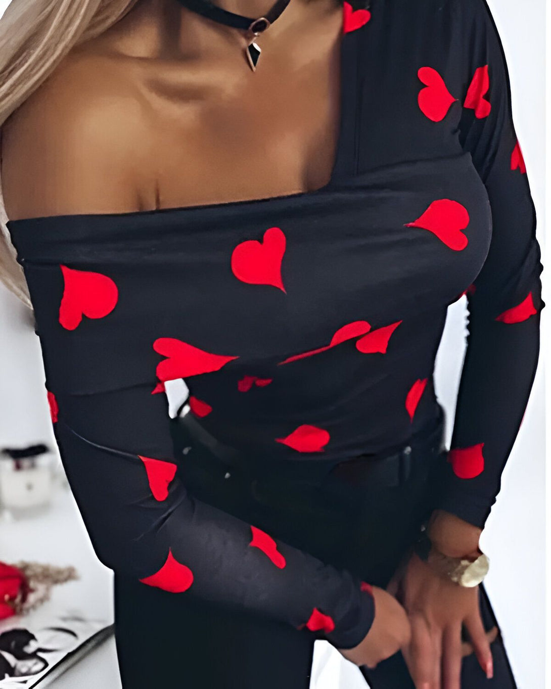 Une femme porte un haut noir à manches longues avec des coeurs rouges. Le haut est décolleté et l'épaule droite est dénudée.