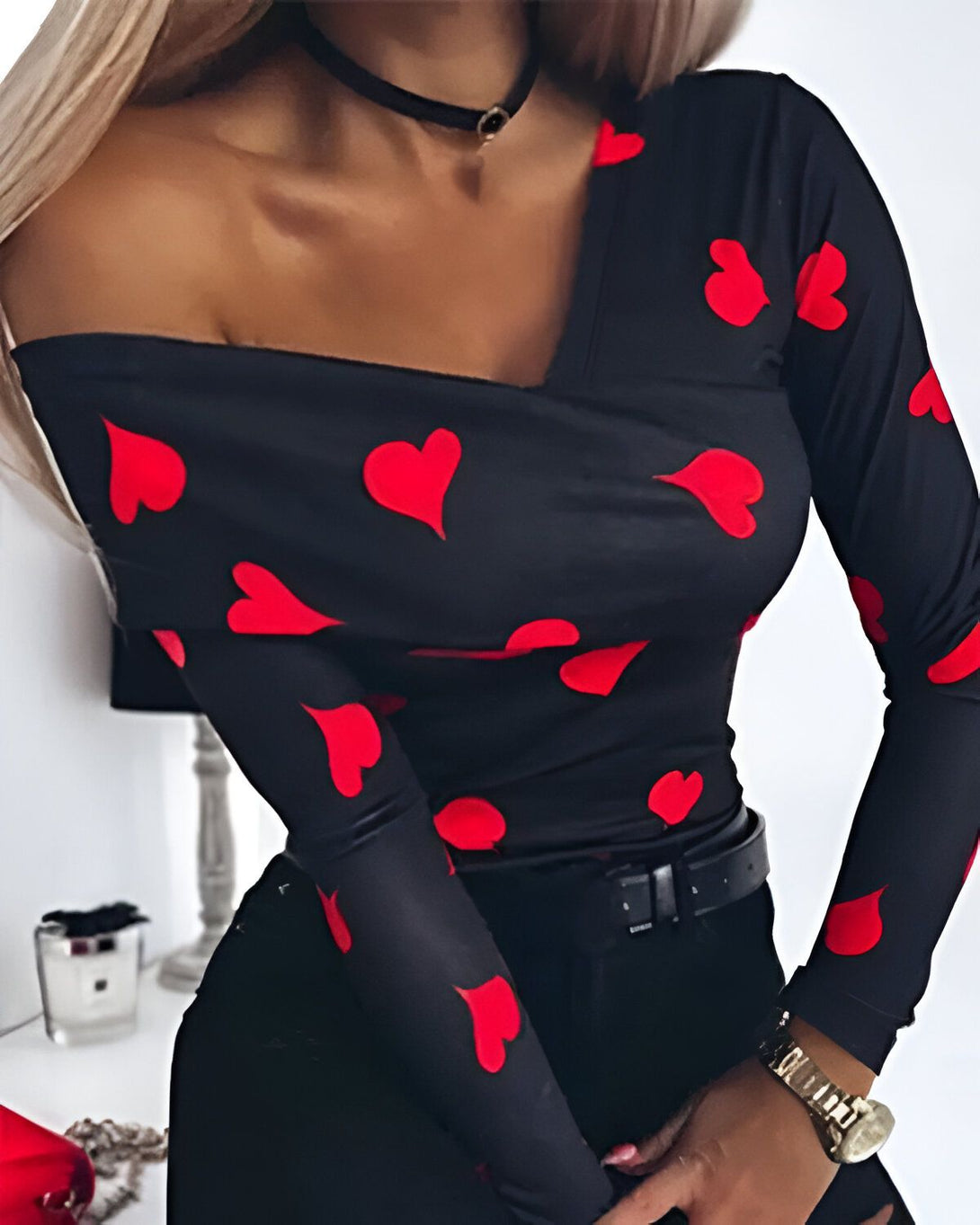 Une femme porte un haut noir à manches longues avec des coeurs rouges. Le haut est décolleté et l'épaule droite est dénudée.