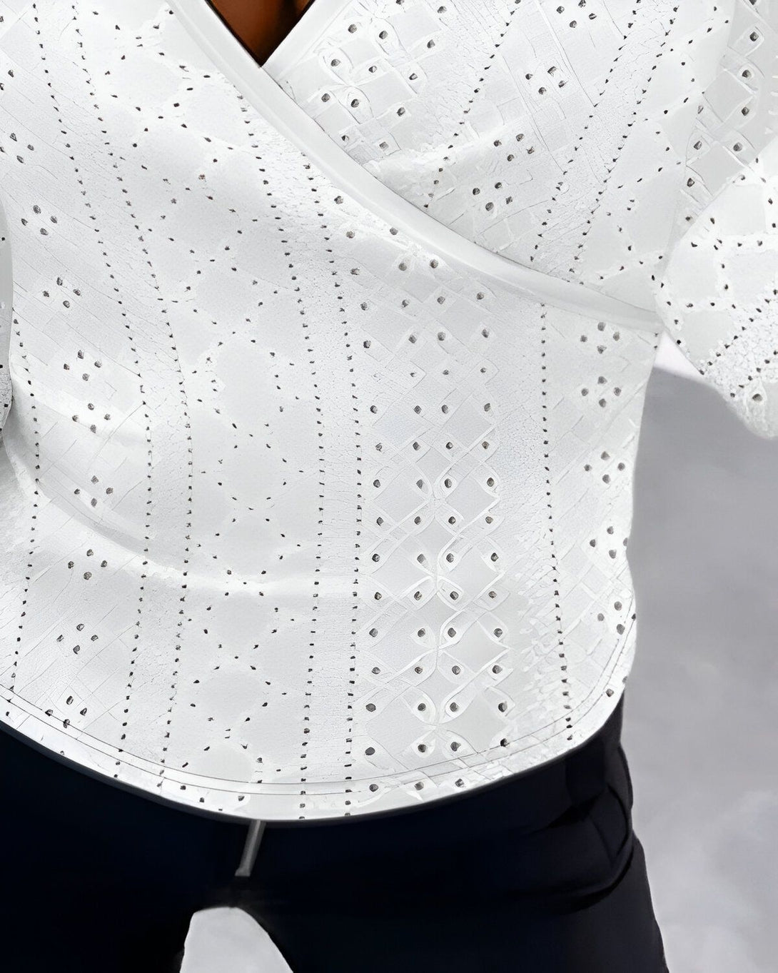 Une image d'un homme portant une chemise blanche à motifs et un pantalon noir. La chemise est ouverte sur le devant et l'homme porte un collier.