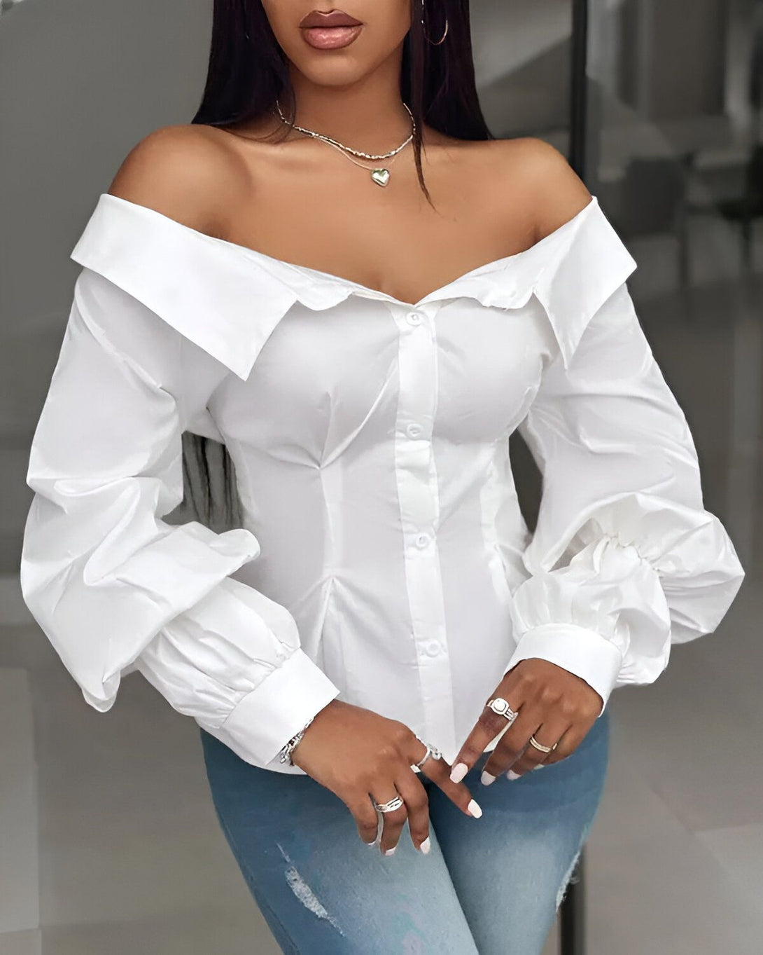 Une femme porte une chemise blanche décolletée et des manches bouffantes. Elle est assortie avec un jean bleu troué.