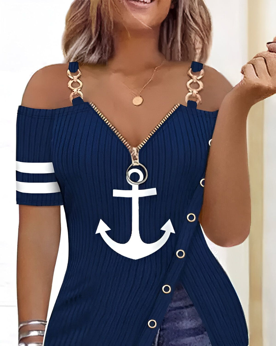 Une femme porte un débardeur bleu marine à épaules dénudées. Le débardeur est zippé sur le devant et comporte une ancre blanche imprimée sur la poitrine. La femme porte également un collier avec un pendentif en forme de pièce de monnaie.