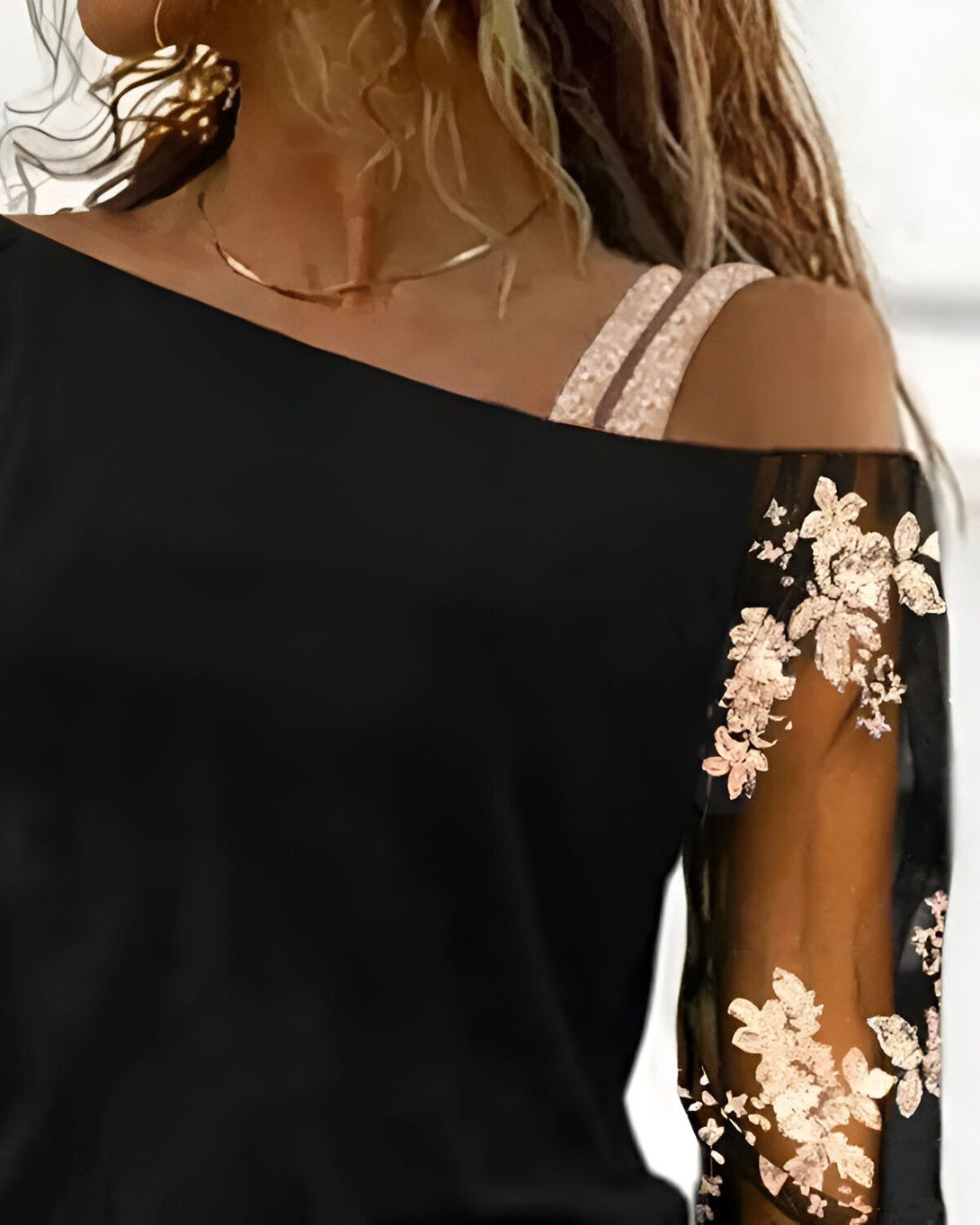 Une image d'une femme portant un haut noir à épaules dénudées avec des fleurs brodées sur la manche.