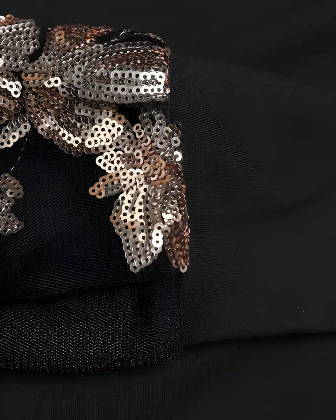 Une image en gros plan d'un tissu noir avec des sequins argentés et dorés cousus dessus. Les sequins sont en forme de fleurs et de feuilles.