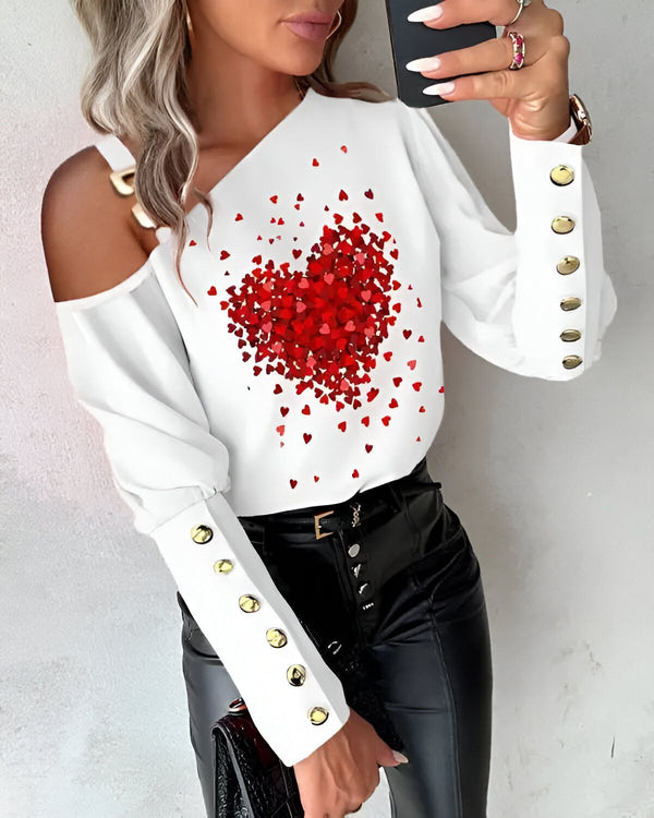Une femme porte un chemisier blanc à épaules dénudées avec un imprimé de cœurs rouges. Le chemisier est rentré dans un pantalon noir. La femme porte également un collier et des boucles d'oreilles.