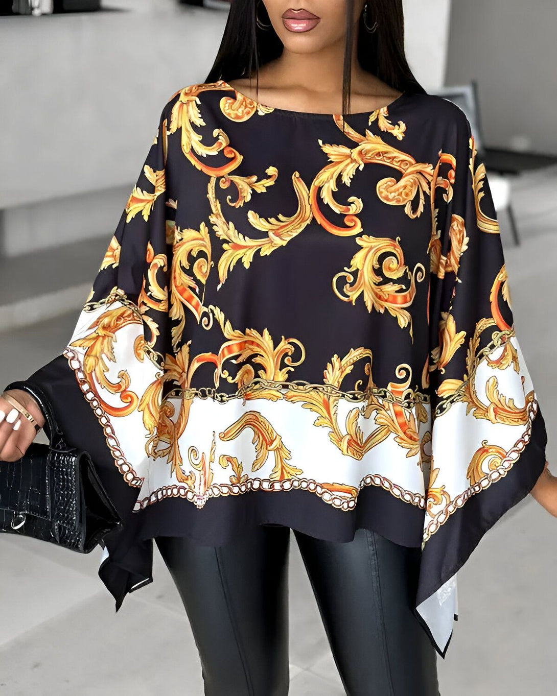 Une femme porte un chemisier noir et doré. Le chemisier est ample et a des manches chauve-souris. Il est imprimé d'un motif floral doré. La femme porte un pantalon noir et des escarpins noirs.