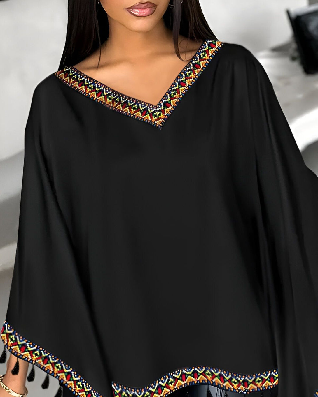Une femme porte un chemisier noir avec des broderies colorées sur le col et les manches.