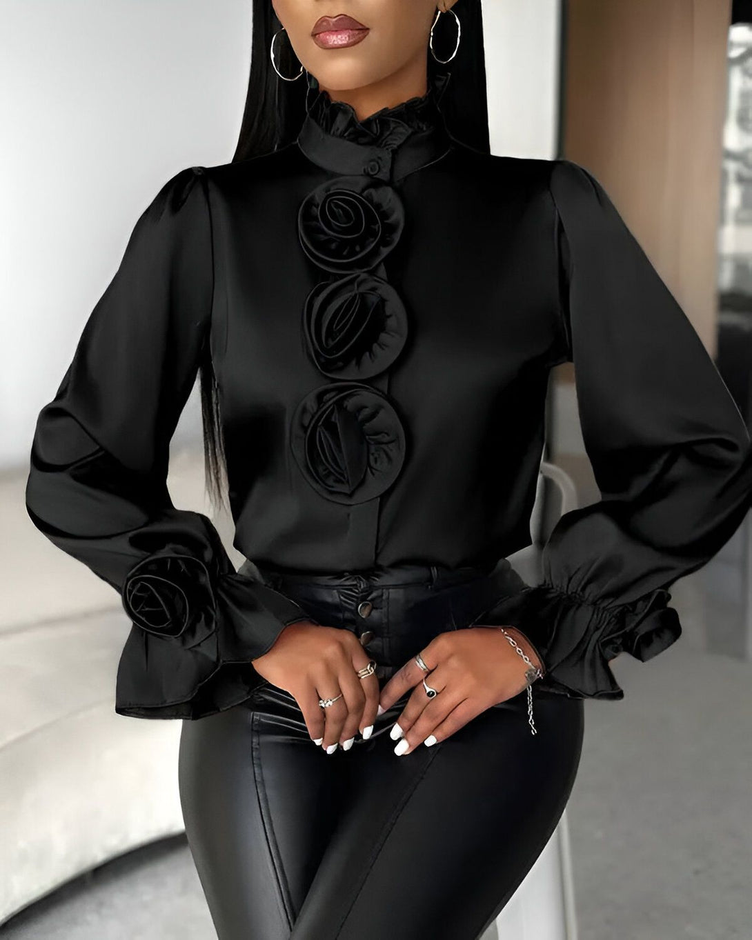Une femme porte un chemisier noir en satin avec des boutons et des manches bouffantes. Le chemisier est orné de roses en satin noir.