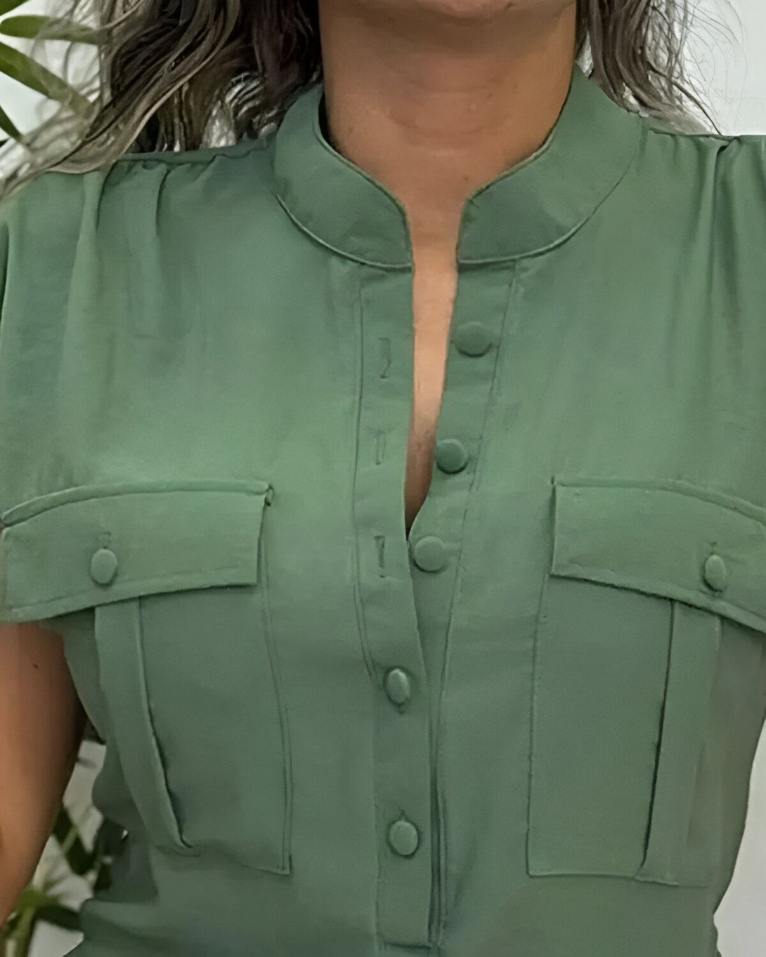 Une femme porte une blouse verte à manches courtes. La blouse est ouverte et on peut voir les boutons.
