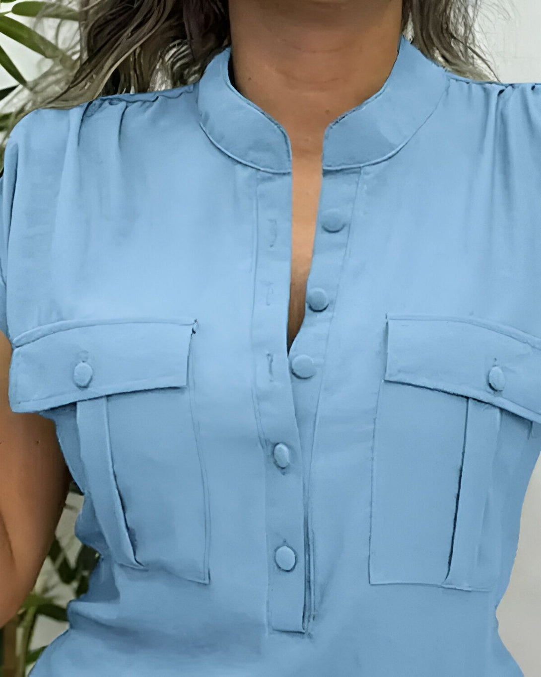 Une image d'une femme portant une chemisier bleu clair. Le chemisier est sans manches et possède un col montant. Il est également doté de deux poches poitrine et de boutons sur le devant.