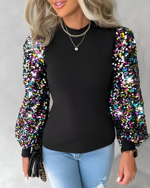 Une femme porte un chemisier noir à manches bouffantes colorées. Le chemisier est rentré dans un jean bleu. La femme porte également un collier avec un pendentif papillon.