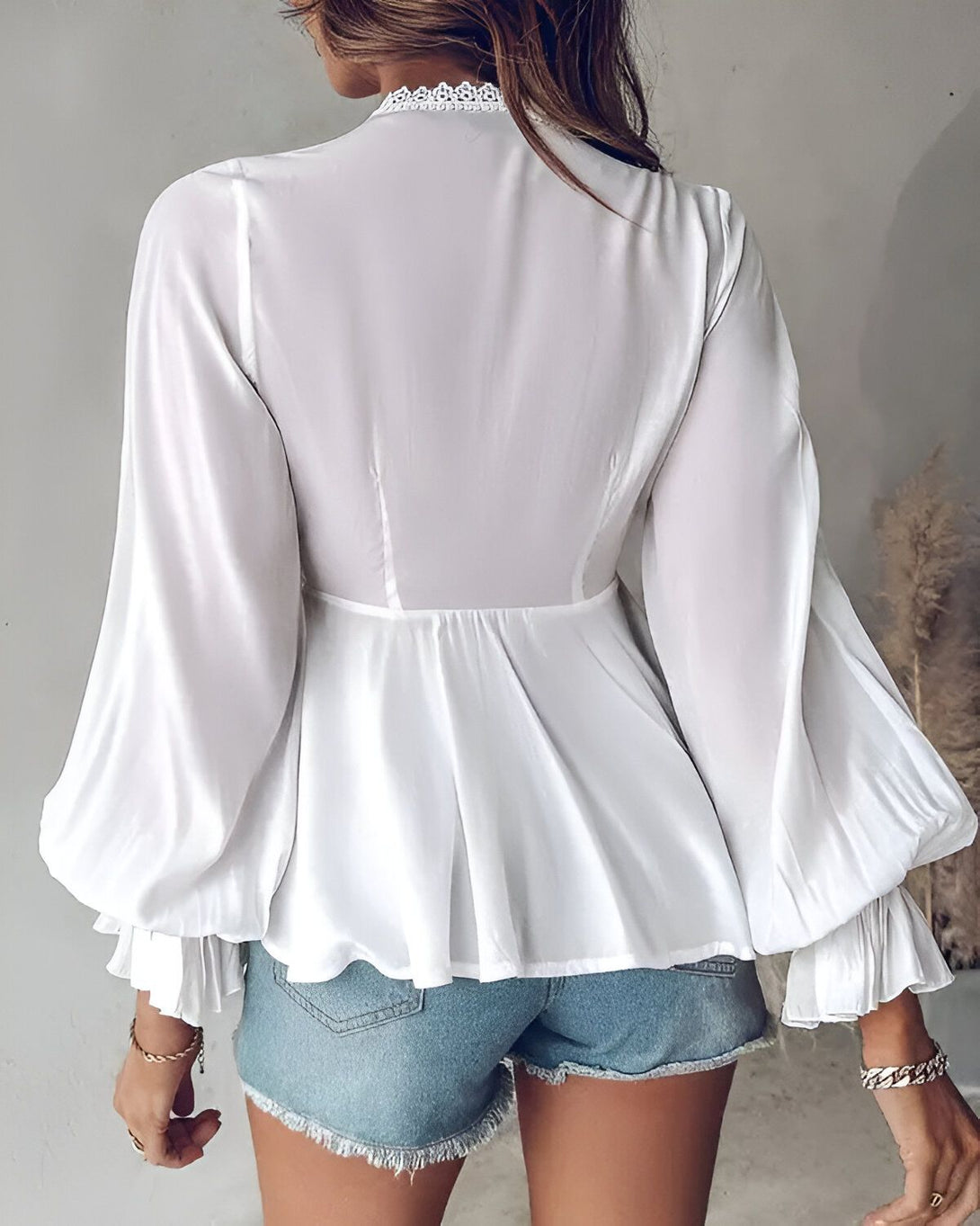 Une femme porte un chemisier blanc avec des manches bouffantes et un col montant en dentelle. Le chemisier est rentré dans un short en jean bleu.