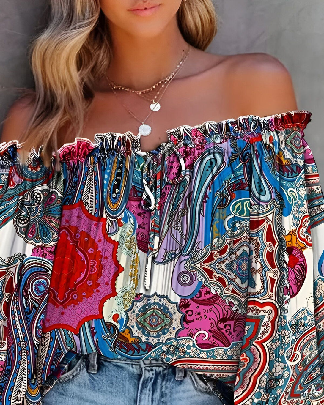 Une jeune femme porte un chemisier à épaules dénudées. Le chemisier est coloré et a un motif cachemire. La femme a les cheveux longs et blonds et porte un collier.