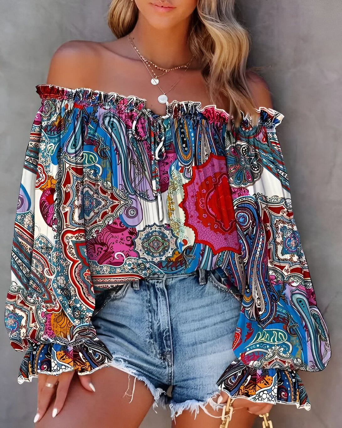 Une femme porte un chemisier à épaules dénudées à motifs cachemire. Le chemisier est bleu, blanc et rouge. La femme est blonde et porte un short en jean.