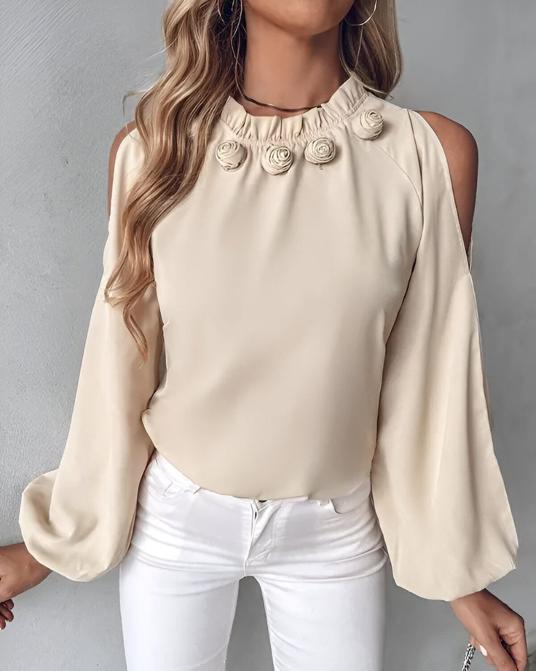 Une jeune femme porte un chemisier beige à épaules dénudées. Le chemisier est orné de boutons en forme de roses.