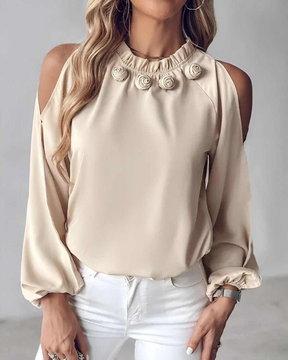 Une jeune femme porte un chemisier beige à épaules dénudées. Le chemisier est orné de roses en tissu sur le col.