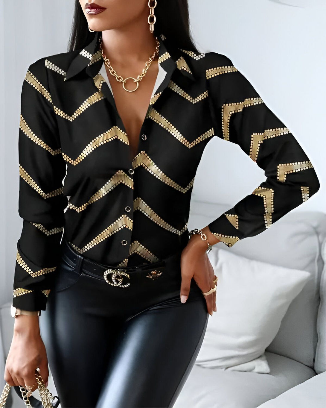 Une femme porte une chemise noire et dorée. La chemise est ouverte et on peut voir son décolleté. Elle porte également un pantalon noir et des talons noirs.