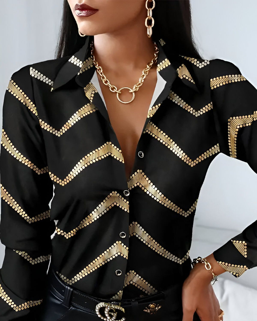 Une femme porte une chemise noire et dorée. La chemise est ouverte et on peut voir son décolleté. Elle porte également un collier doré.