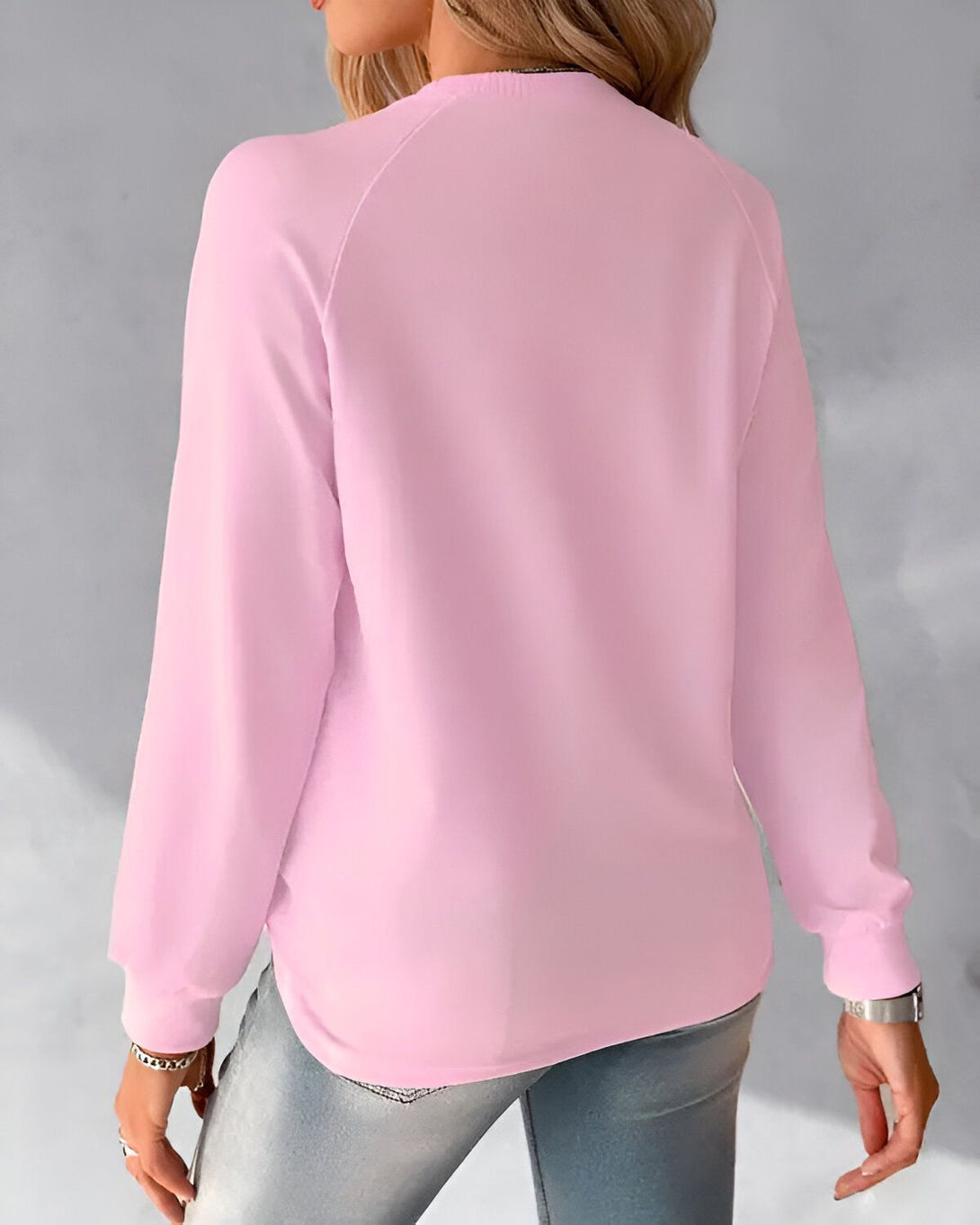 Une femme porte un sweat-shirt rose à manches longues et un jean bleu.