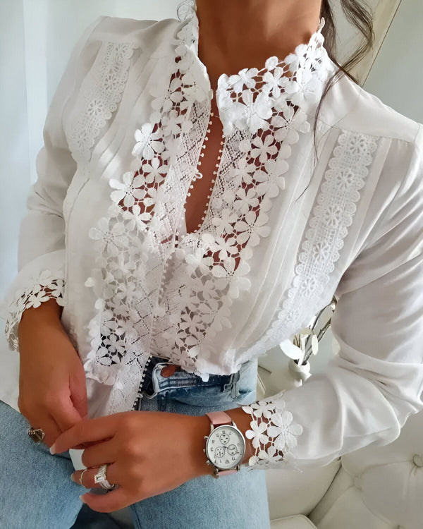 Une femme porte un chemisier blanc en dentelle. Le chemisier est cintré et possède un col montant. La femme porte également un jean bleu et une montre rose.