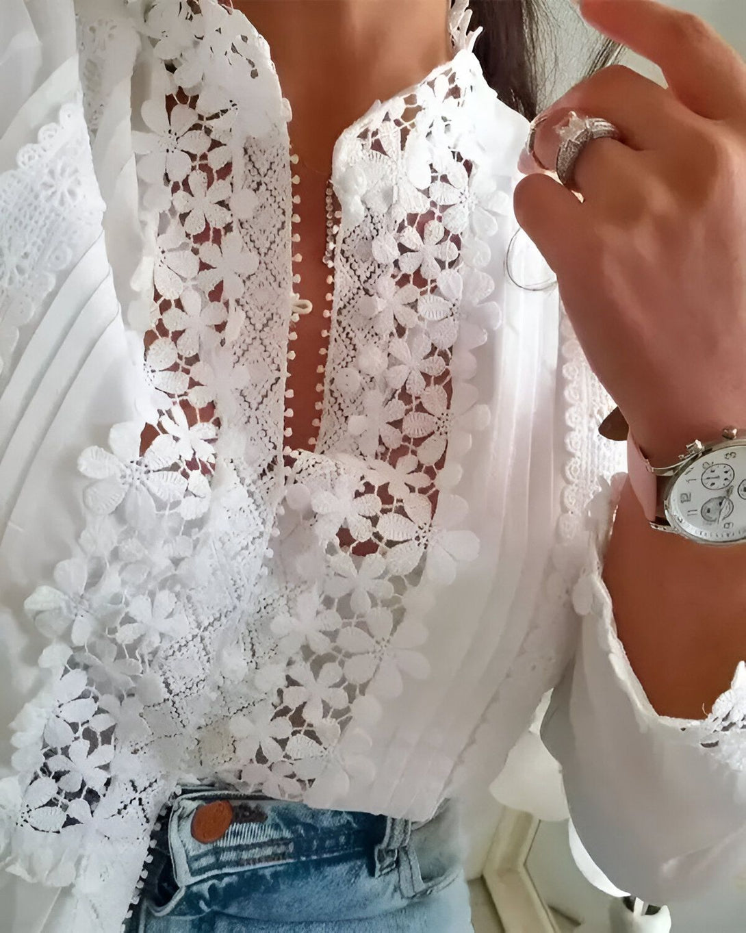 Une image d'une femme portant un chemisier blanc en dentelle. Le chemisier est décolleté et possède des manches longues. La femme porte également un jean bleu et une montre rose.