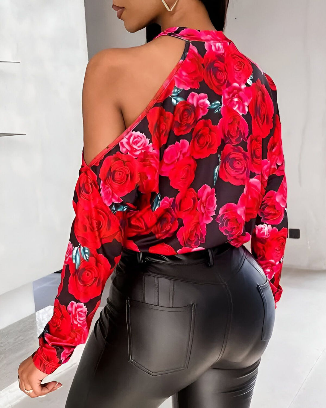 Une femme porte un chemisier rouge et noir à une épaule avec un pantalon en cuir noir.