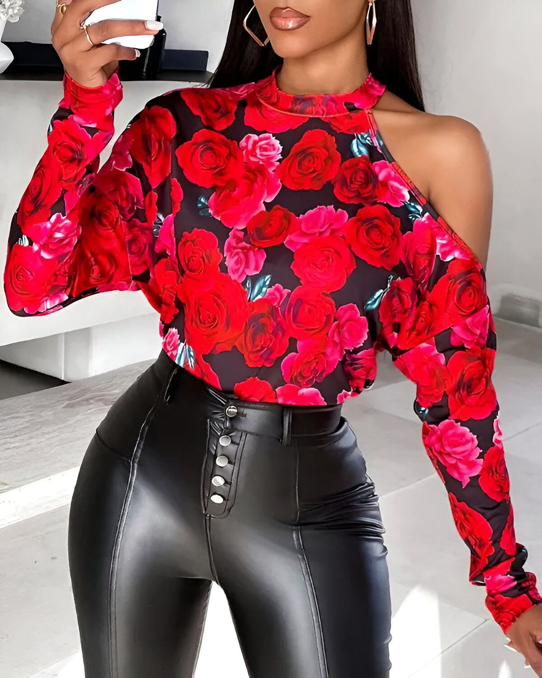 Une femme porte un chemisier noir à col montant et à une manche avec des roses rouges. Le chemisier est porté avec un pantalon en cuir noir.