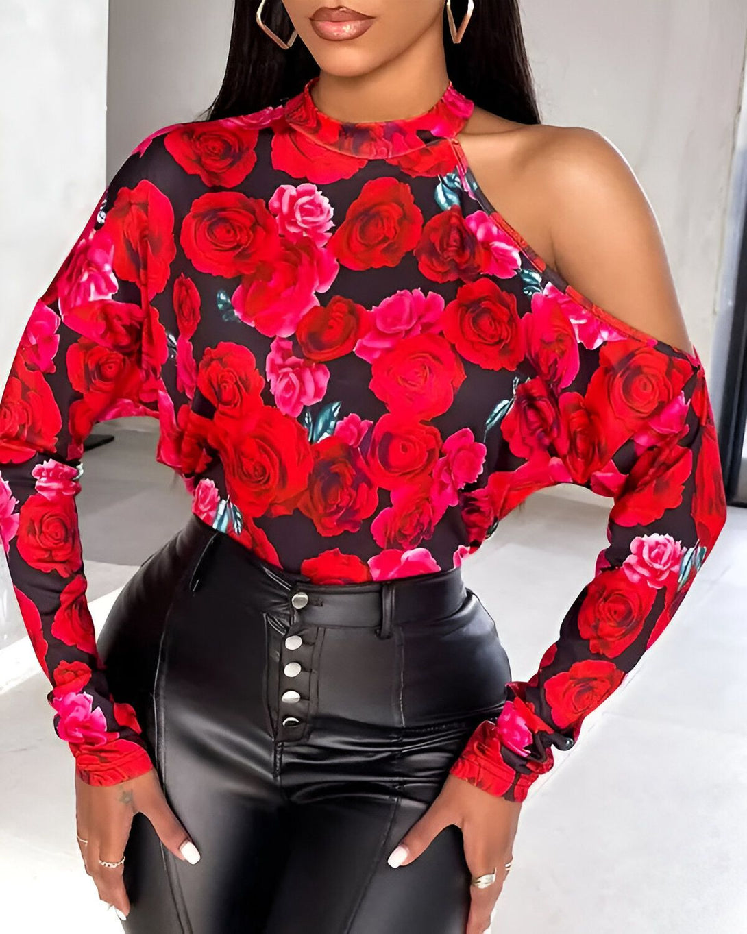Une femme porte un chemisier noir à col montant et à une manche avec des roses rouges. Le chemisier est porté avec un pantalon en cuir noir.