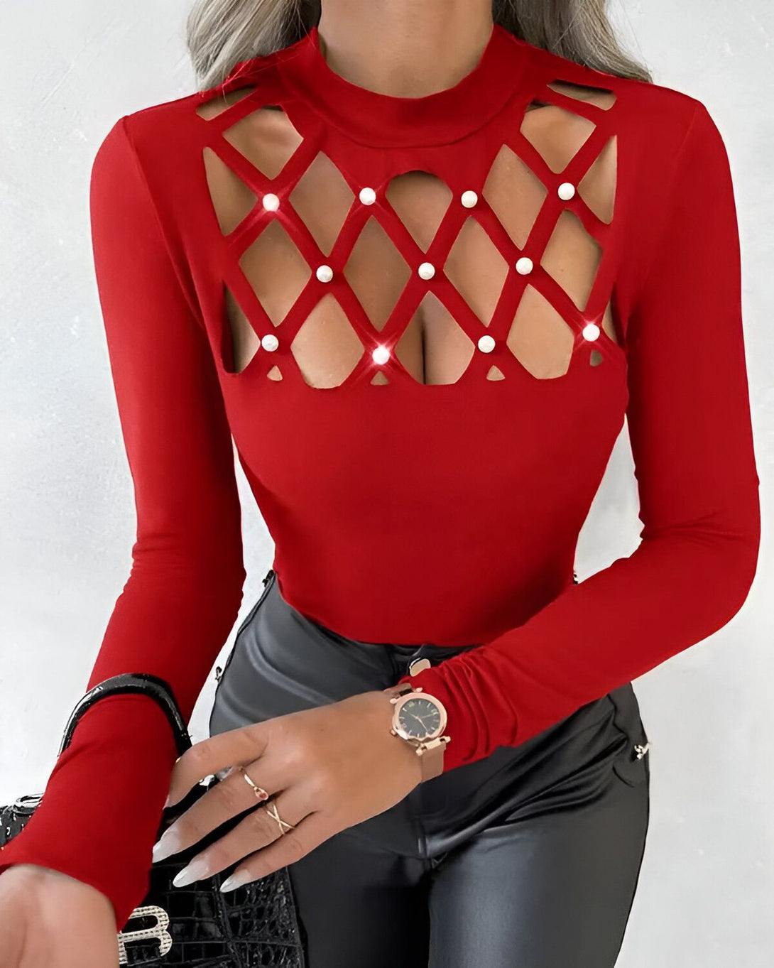 Une femme porte un chemisier rouge moulant à manches longues. Le chemisier est orné de perles et de strass.