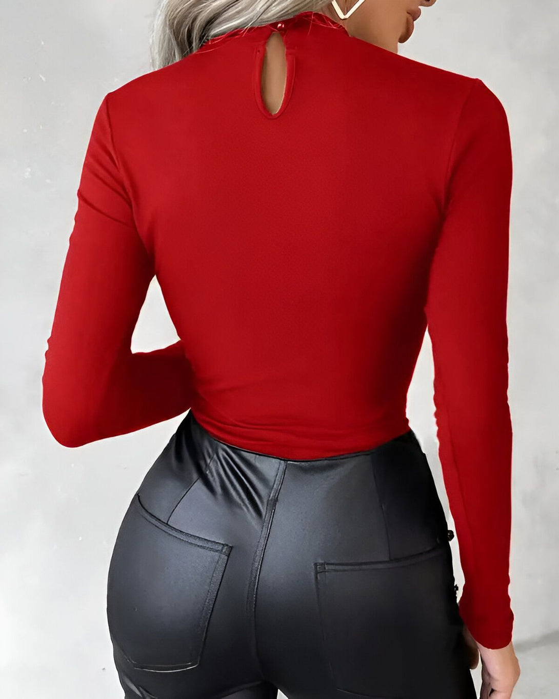 Une femme porte un haut rouge moulant à manches longues et un pantalon en cuir noir.