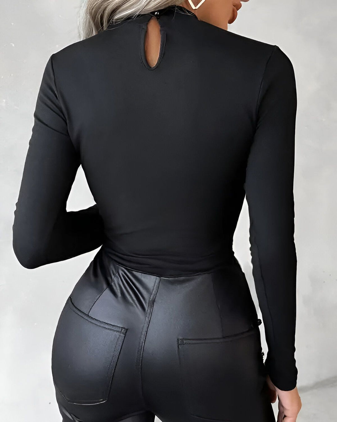 Une femme porte un body noir moulant à col montant et des pantalons en cuir noir.