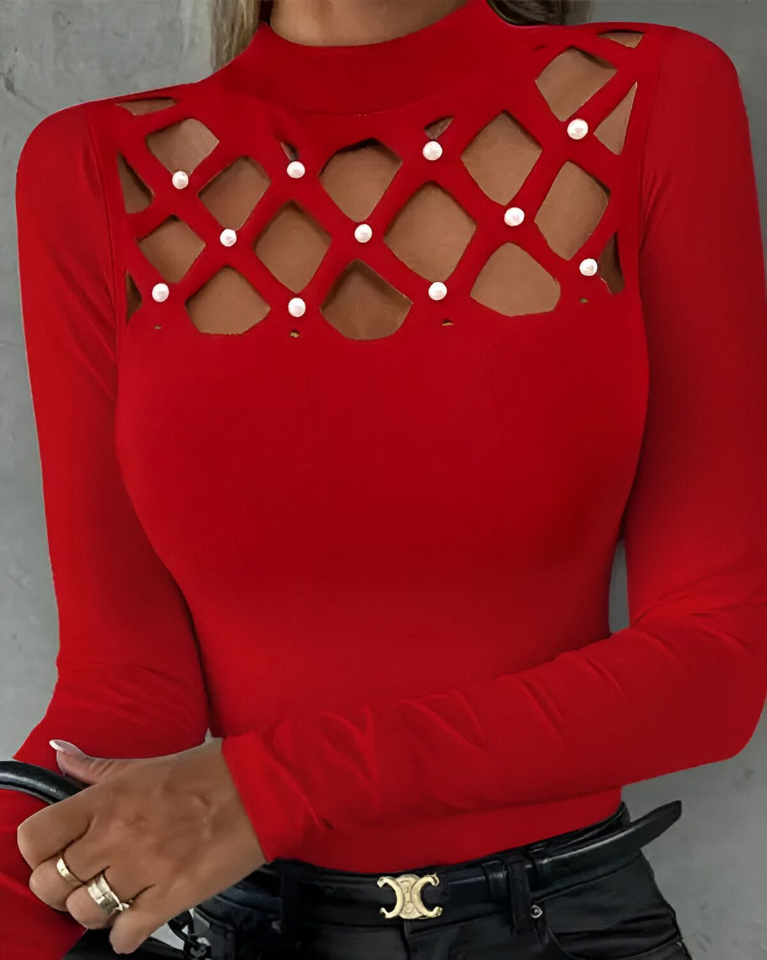 Une femme porte un haut rouge à manches longues avec un col montant. Le haut est ajouré au niveau de la poitrine et des perles blanches sont présentes sur les contours de l'ouverture.
