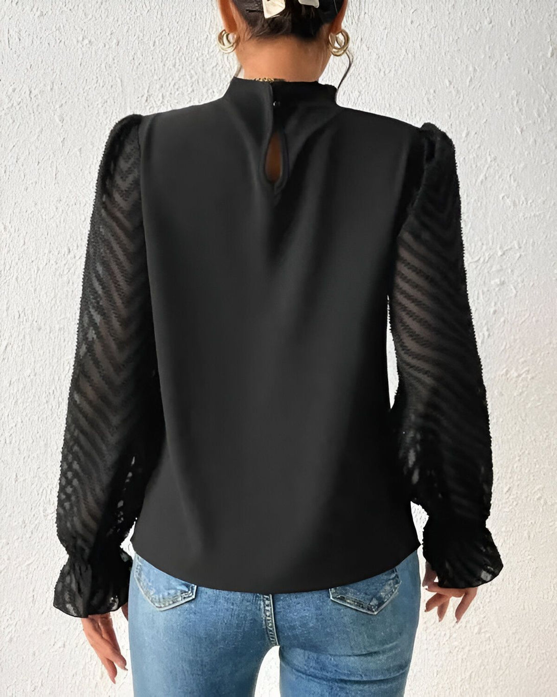 Une femme porte un chemisier noir avec des manches bouffantes transparentes à motifs zébrés.