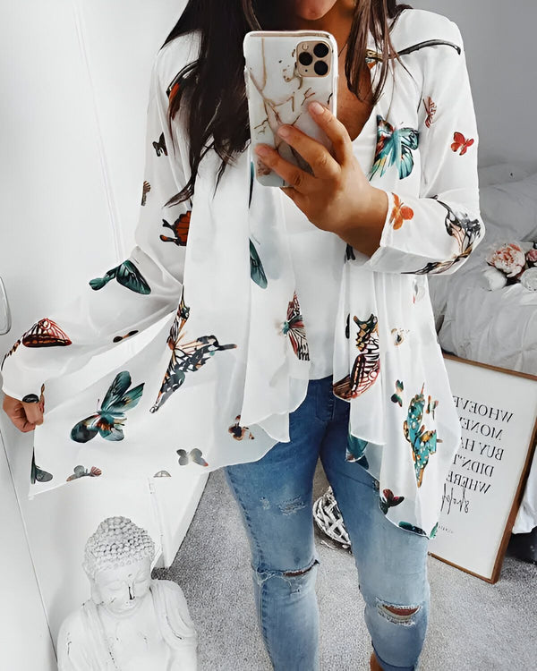 Une femme porte un kimono blanc à motifs papillons. Elle est debout devant un miroir et tient son téléphone dans la main.