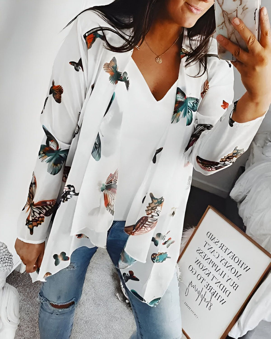 Une femme porte un kimono blanc avec des motifs papillons multicolores. Elle porte également un t-shirt blanc et un jean bleu déchiré.