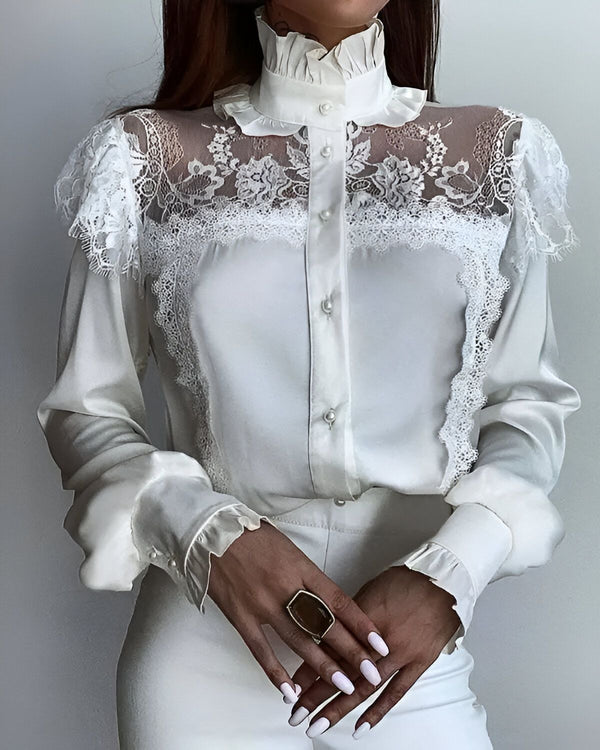 Une femme porte un chemisier blanc en dentelle. Le chemisier est transparent au niveau des épaules et du cou. Il est boutonné sur le devant. La femme porte également un pantalon blanc. Elle a les cheveux longs et noirs. Elle est maquillée et porte du vernis à ongles blanc.