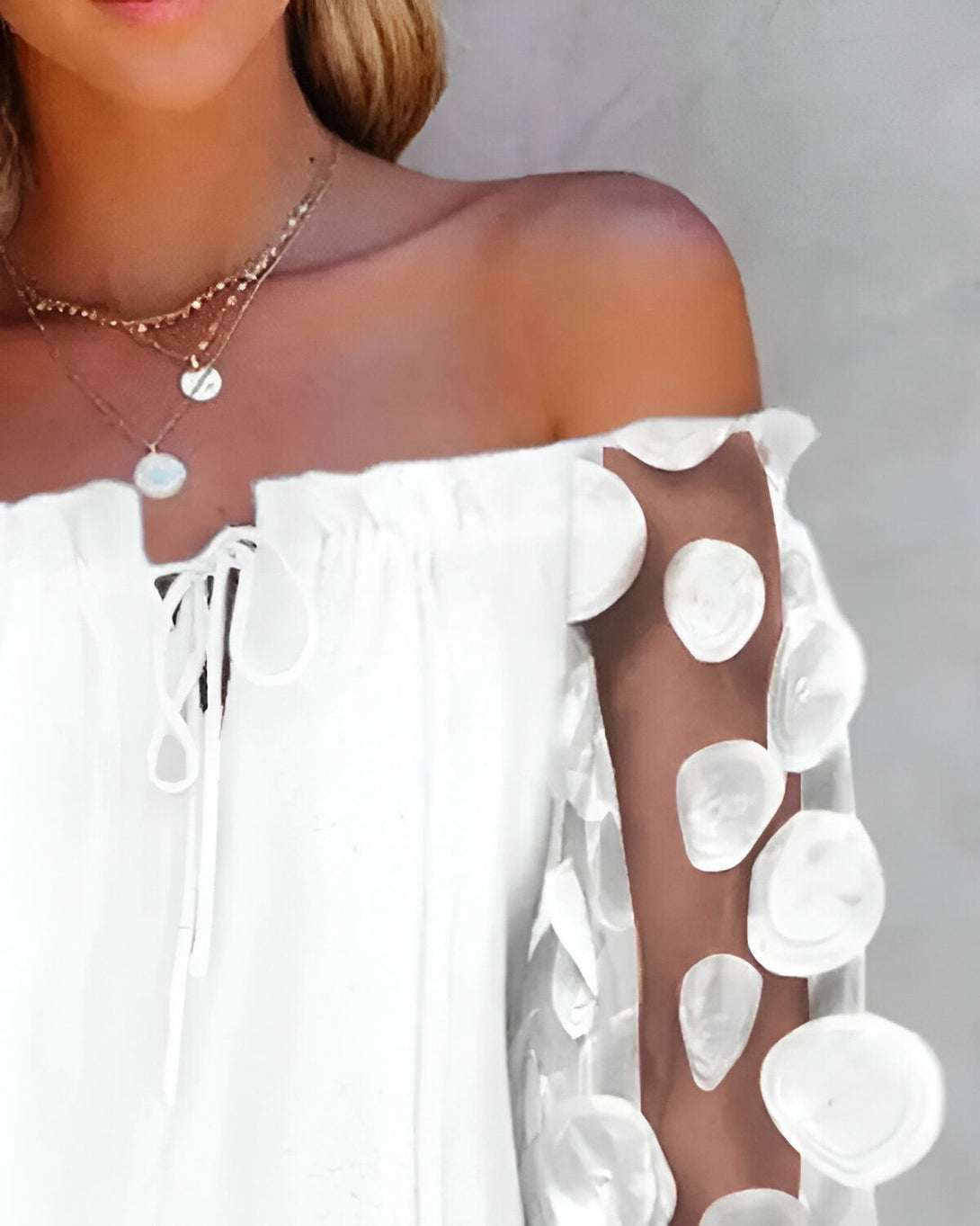 Une jeune femme porte une blouse blanche à épaules dénudées. La blouse est ornée de fleurs en relief sur les manches.