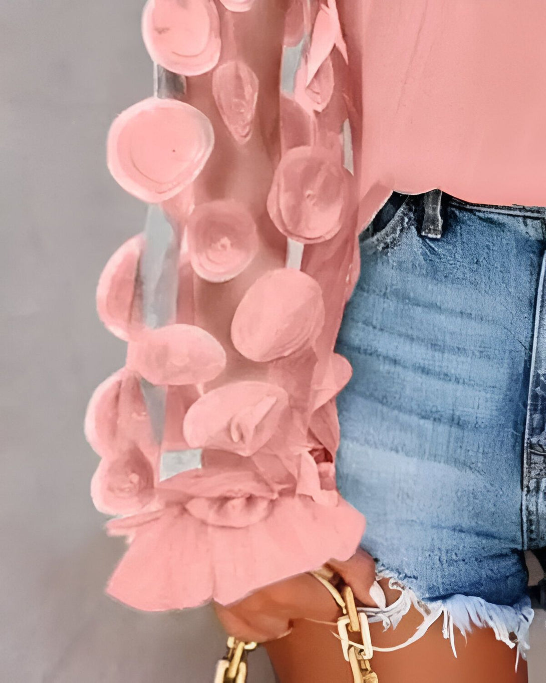 Une femme porte un chemisier rose à manches bouffantes et un jean bleu déchiré.